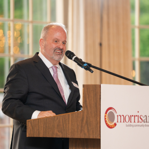 Tom Werder in a suite standing at a podium speaking into a microphone.