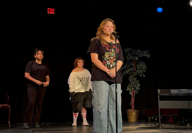 Photo of a teen girl standing in front of a microphone on stage.