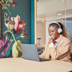 Woman sits in front of a laptop in an office at Sanofi's new Morristown location with a colorful mural in the background.